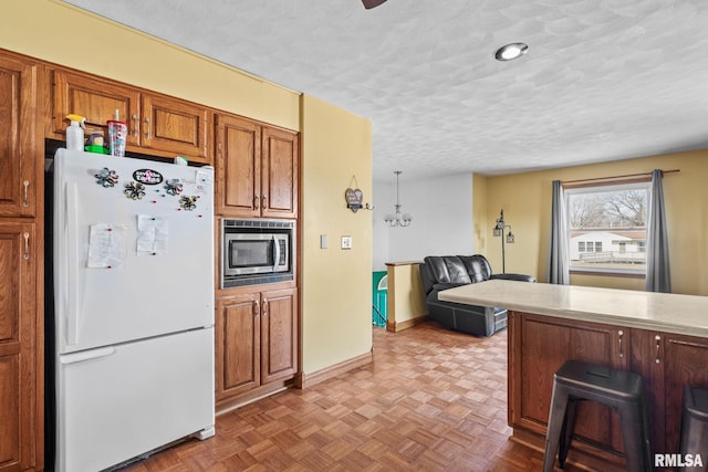 kitchen with brown cabinets, stainless steel microwave, freestanding refrigerator, a textured ceiling, and a kitchen breakfast bar