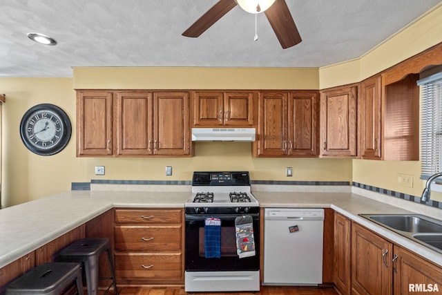 kitchen with white dishwasher, under cabinet range hood, a sink, range with gas stovetop, and brown cabinetry