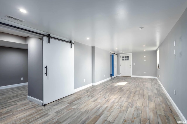 empty room featuring a barn door, baseboards, visible vents, wood finished floors, and recessed lighting