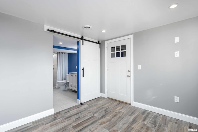 entrance foyer with a barn door, baseboards, visible vents, wood finished floors, and recessed lighting