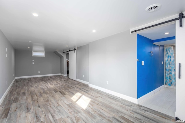 basement featuring wood finished floors, visible vents, baseboards, and a barn door