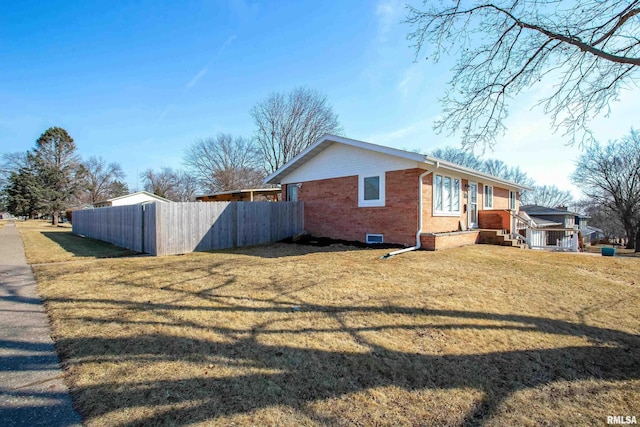 view of side of home featuring brick siding, crawl space, fence, and a lawn