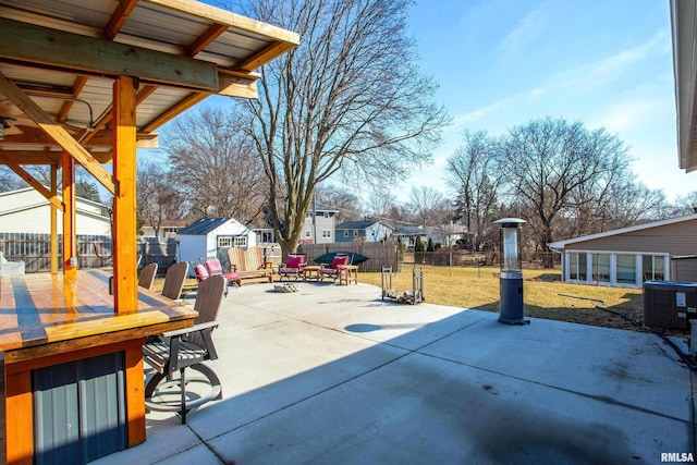 view of patio with an outbuilding, a storage shed, central AC unit, a fenced backyard, and a fire pit