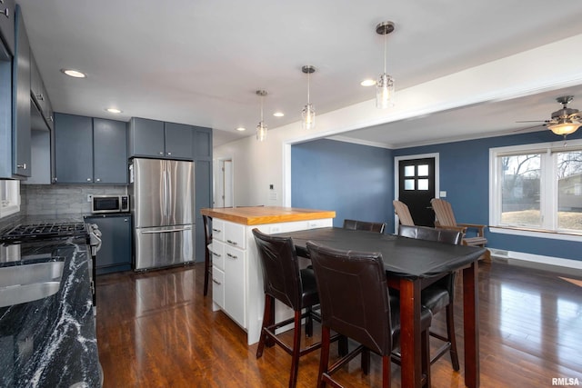 kitchen featuring dark wood-style floors, hanging light fixtures, decorative backsplash, appliances with stainless steel finishes, and baseboards