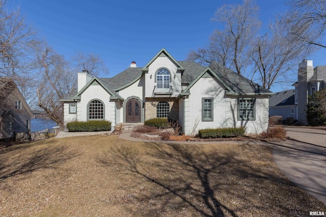 french country inspired facade featuring stone siding, a chimney, and stucco siding