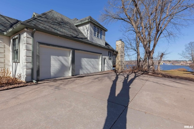 view of home's exterior with concrete driveway, stucco siding, an attached garage, and a water view