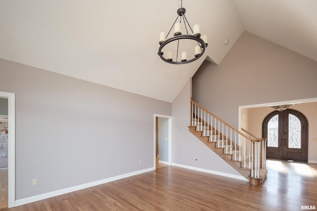 unfurnished living room with baseboards, stairway, wood finished floors, an inviting chandelier, and french doors