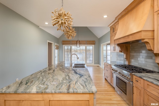 kitchen with decorative backsplash, lofted ceiling, custom range hood, high end stainless steel range, and a sink