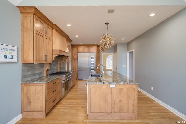 kitchen with premium appliances, tasteful backsplash, light wood-style flooring, a sink, and an island with sink