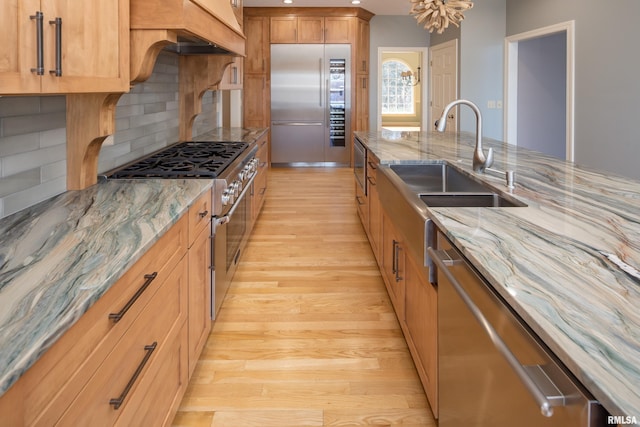 kitchen with tasteful backsplash, high end appliances, light wood-style flooring, light stone countertops, and a sink