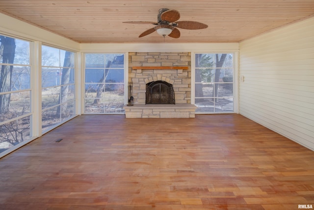 unfurnished living room featuring wooden ceiling, a ceiling fan, wood finished floors, and a stone fireplace