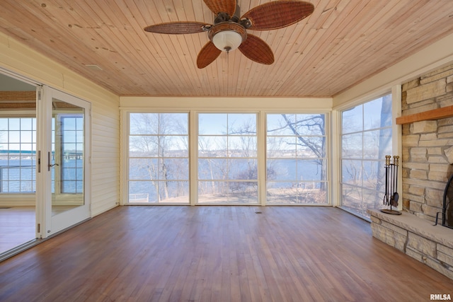 unfurnished sunroom featuring a ceiling fan, wood ceiling, and a stone fireplace