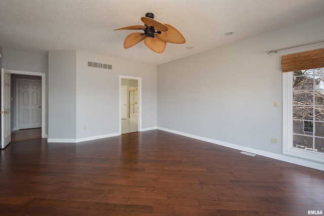 empty room featuring dark wood-style floors, ceiling fan, visible vents, and baseboards