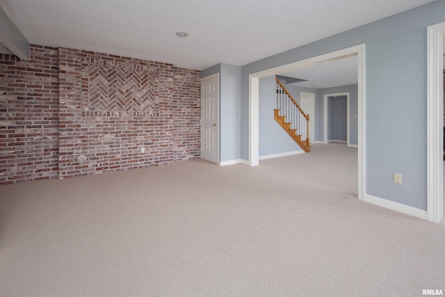 empty room with stairs, brick wall, a textured ceiling, and baseboards