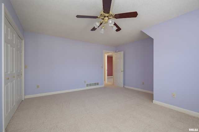 unfurnished bedroom featuring baseboards, visible vents, light colored carpet, a textured ceiling, and a closet