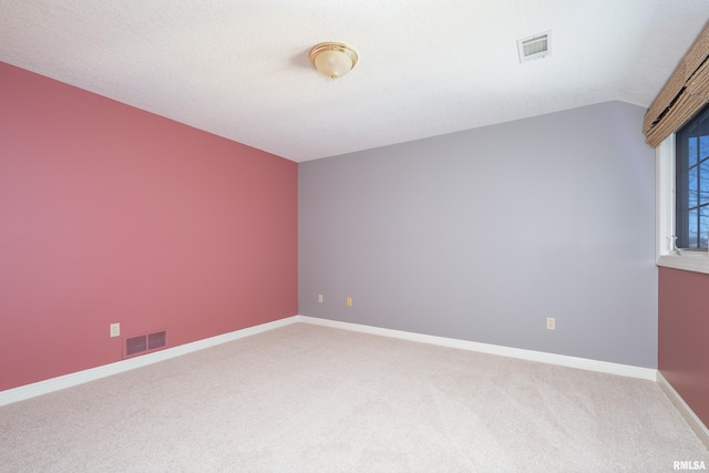 carpeted empty room featuring lofted ceiling, a textured ceiling, visible vents, and baseboards