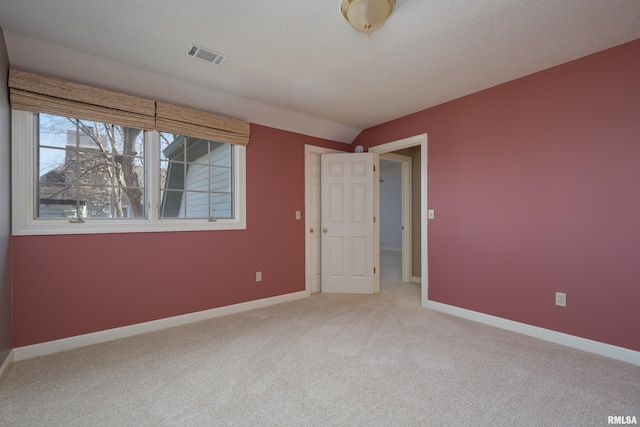 empty room with light carpet, vaulted ceiling, visible vents, and baseboards