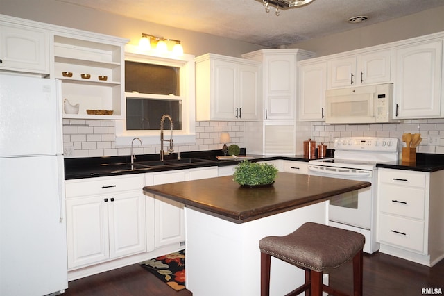 kitchen featuring dark countertops, white appliances, white cabinets, and a sink