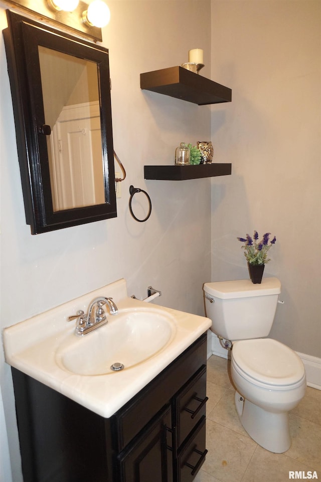 half bath with toilet, tile patterned floors, baseboards, and vanity