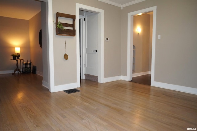 empty room featuring arched walkways, baseboards, crown molding, and light wood finished floors