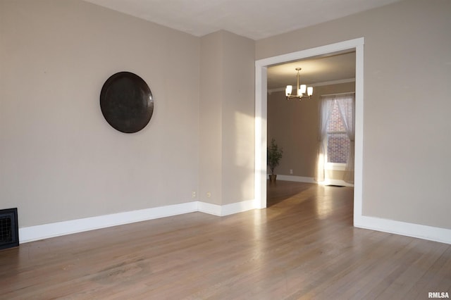 spare room with a notable chandelier, baseboards, and wood finished floors