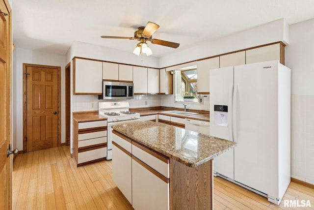 kitchen with white appliances, a sink, white cabinetry, light wood-type flooring, and a center island