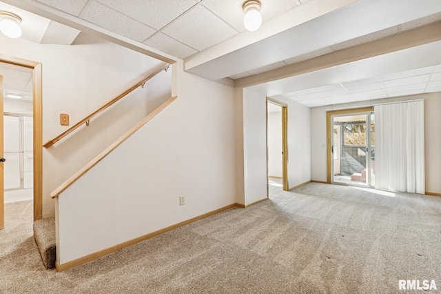 below grade area with stairs, carpet flooring, a paneled ceiling, and baseboards