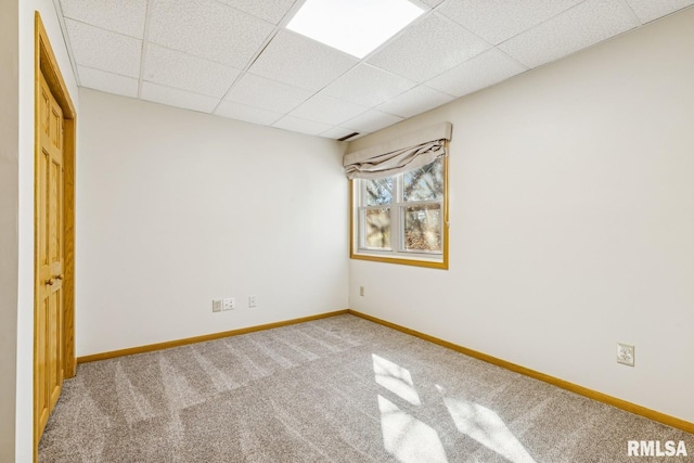 empty room with carpet flooring, a paneled ceiling, and baseboards