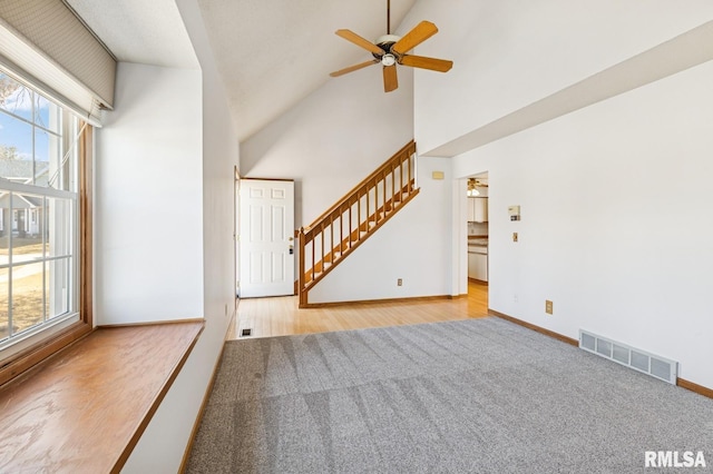 unfurnished living room with visible vents, stairway, a ceiling fan, high vaulted ceiling, and baseboards