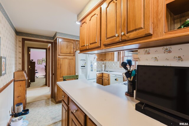 kitchen featuring a sink, light countertops, brown cabinets, white fridge with ice dispenser, and wallpapered walls