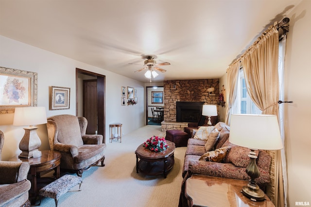 carpeted living area featuring a ceiling fan and a stone fireplace