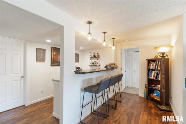 kitchen featuring dark wood-style flooring, baseboards, a textured ceiling, and a breakfast bar area