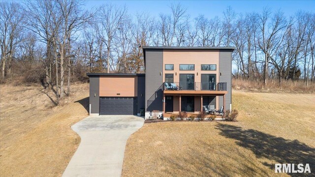 contemporary house featuring driveway, a balcony, an attached garage, and a front lawn