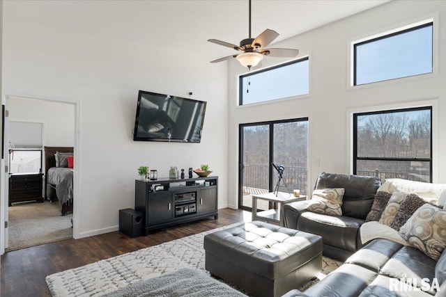 living area with dark wood-style flooring, a towering ceiling, a ceiling fan, and baseboards