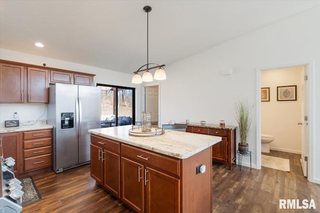 kitchen featuring stainless steel fridge, dark wood finished floors, a kitchen island, light stone counters, and decorative light fixtures