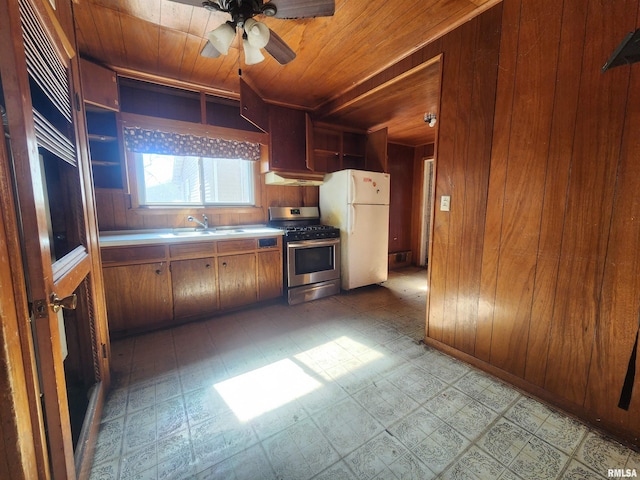 kitchen featuring wooden ceiling, wooden walls, freestanding refrigerator, stainless steel gas stove, and light floors