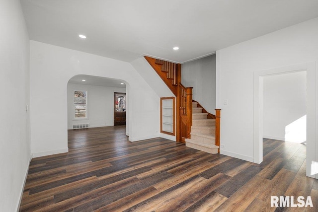 unfurnished room featuring visible vents, arched walkways, dark wood-style floors, stairs, and recessed lighting