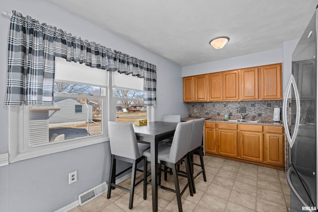 kitchen with visible vents, backsplash, brown cabinetry, freestanding refrigerator, and a sink