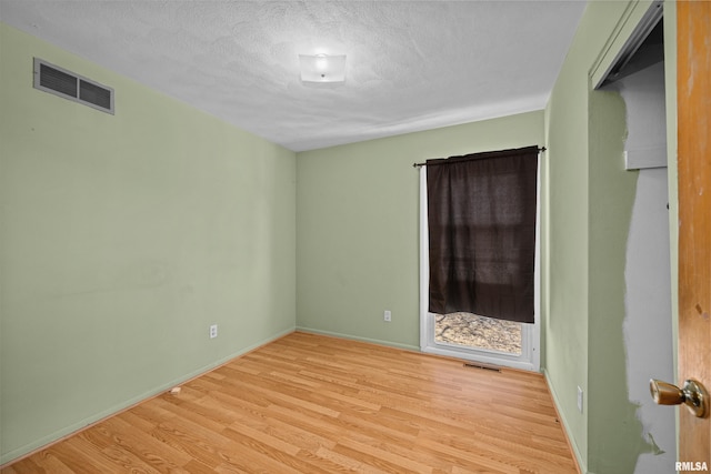 empty room with light wood-style floors, visible vents, a textured ceiling, and baseboards