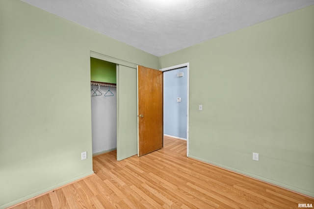 unfurnished bedroom with a textured ceiling, a closet, wood finished floors, and baseboards