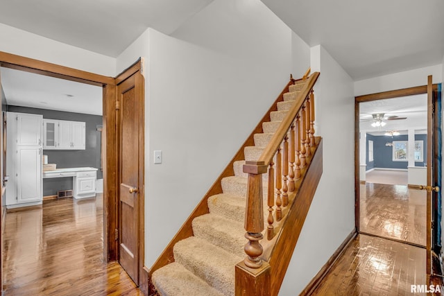 stairway with built in desk, ceiling fan, baseboards, and hardwood / wood-style floors