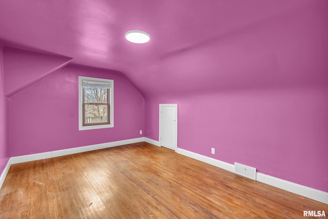 additional living space with vaulted ceiling, wood finished floors, visible vents, and baseboards