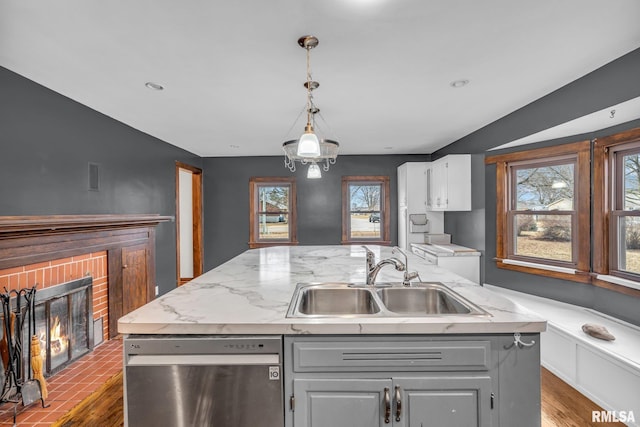 kitchen featuring gray cabinetry, a sink, a brick fireplace, dishwasher, and a center island with sink