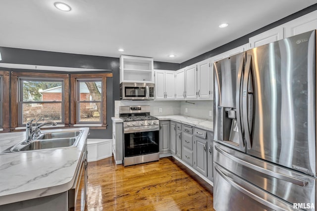 kitchen with recessed lighting, gray cabinetry, stainless steel appliances, a sink, and light wood-type flooring