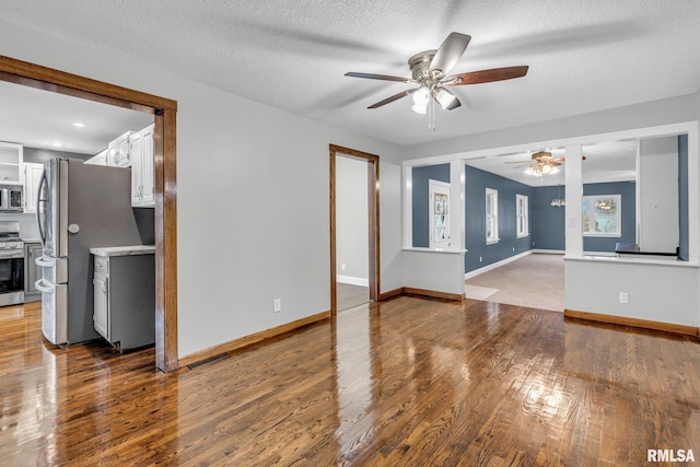 unfurnished living room with a textured ceiling, wood finished floors, visible vents, and baseboards