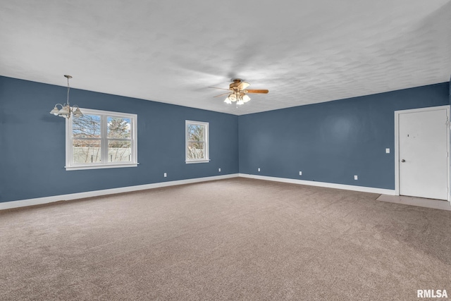 spare room with carpet, baseboards, and ceiling fan with notable chandelier