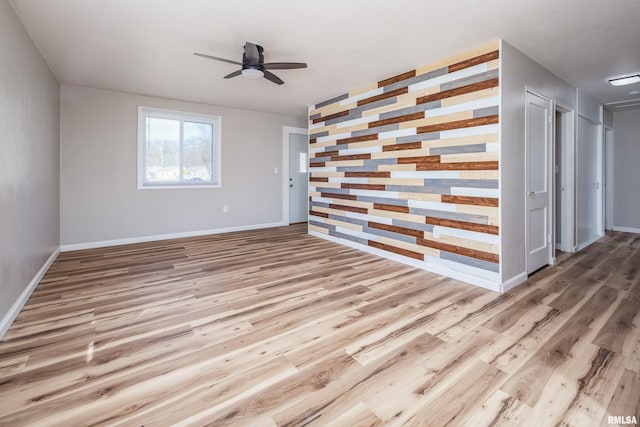 spare room with an accent wall, ceiling fan, baseboards, and wood finished floors