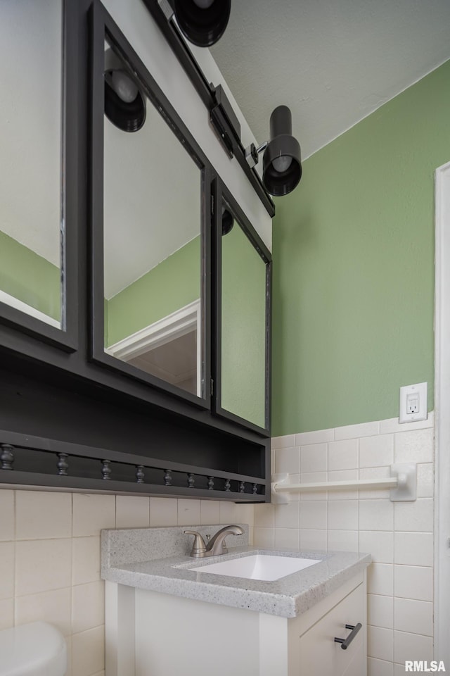 half bathroom featuring wainscoting, toilet, tile walls, and vanity