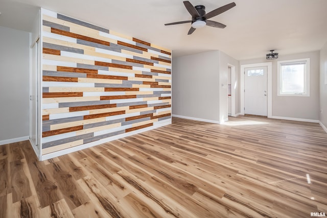 unfurnished living room featuring an accent wall, a ceiling fan, baseboards, and wood finished floors