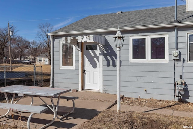 property entrance with fence, a patio, and roof with shingles